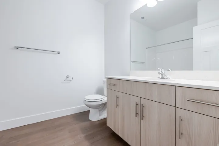 Wood-finish flooring, white walls, and a light wood-finish vanity with a white countertop