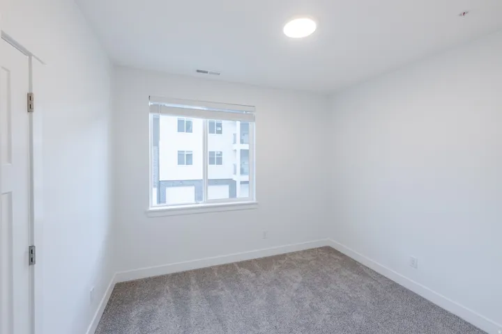 Neutral white wall paint, grey carpet flooring, recessed ceiling light fixture, and a white framed window