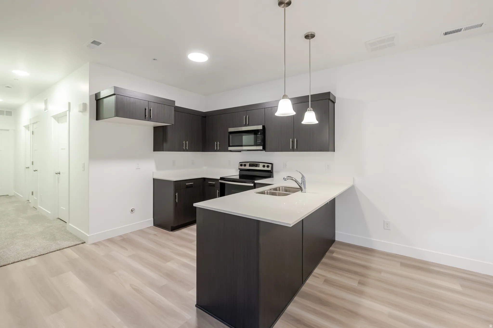 Kitchen featuring dark wood-finish cabinetry, light countertops, stainless steel appliances, and pendant lighting