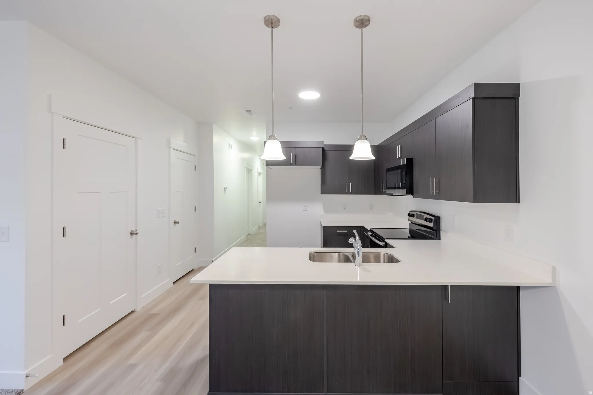 Modern kitchen featuring dark wood-finish cabinetry, light-toned countertops, and stainless steel appliances
