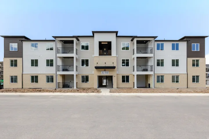 Modern multi-story building featuring light-colored siding, brick accents, and black trim