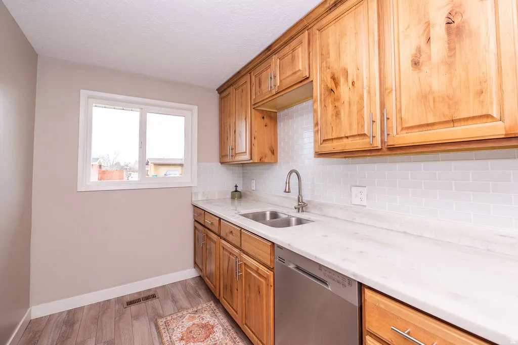 Kitchen featuring dishwasher, light wood-style floors, light stone counters, backsplash, and wood finish cabinets