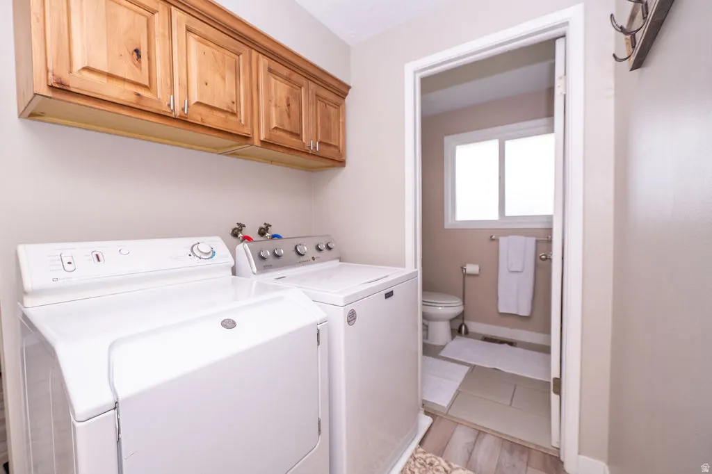Laundry room with independent washer and dryer, cabinet space, and light wood-style floors