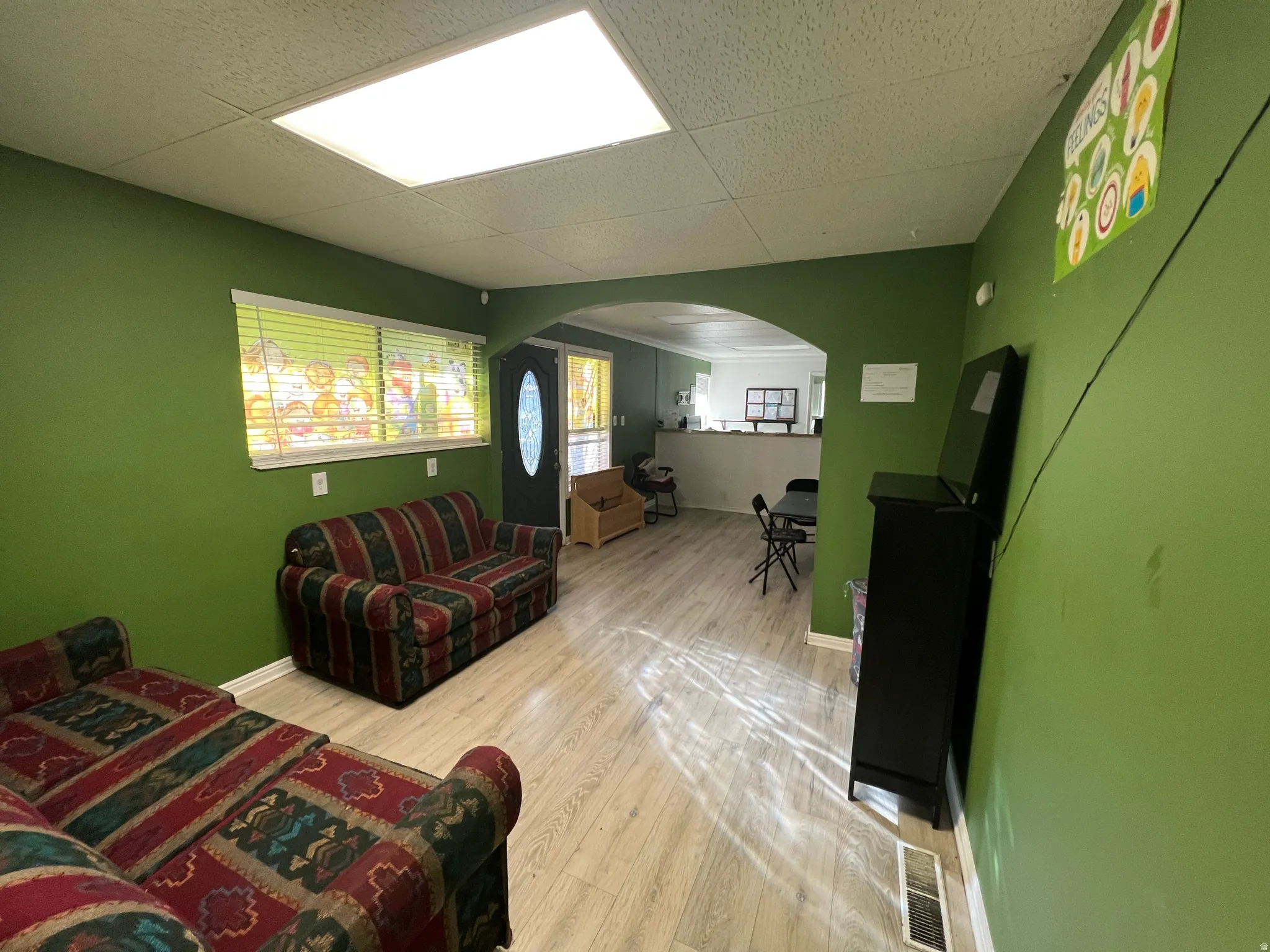 Living area with arched walkways, light wood-style floors, and a paneled ceiling