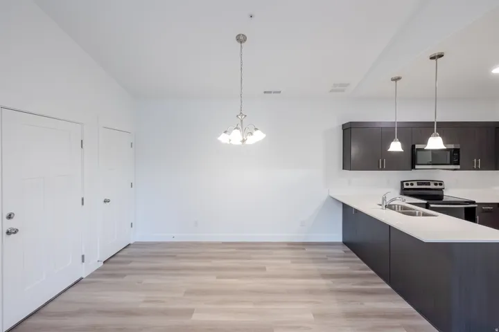 Wood-finish flooring throughout, bright white walls, modern dark wood cabinetry, white countertops, and stainless steel appliances