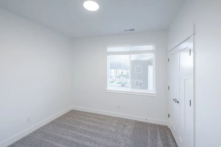Recessed ceiling light fixture, white walls, gray carpet flooring, window with blinds, and white paneled doors
