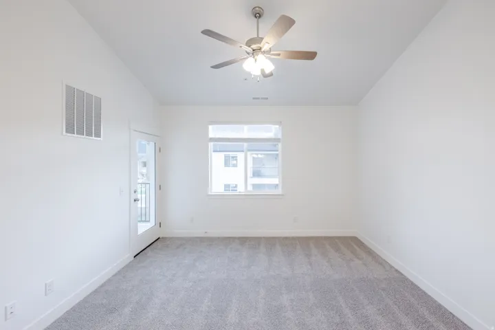 Light gray carpeting, white walls, ceiling fan with light fixture, and a glass-paneled exterior door