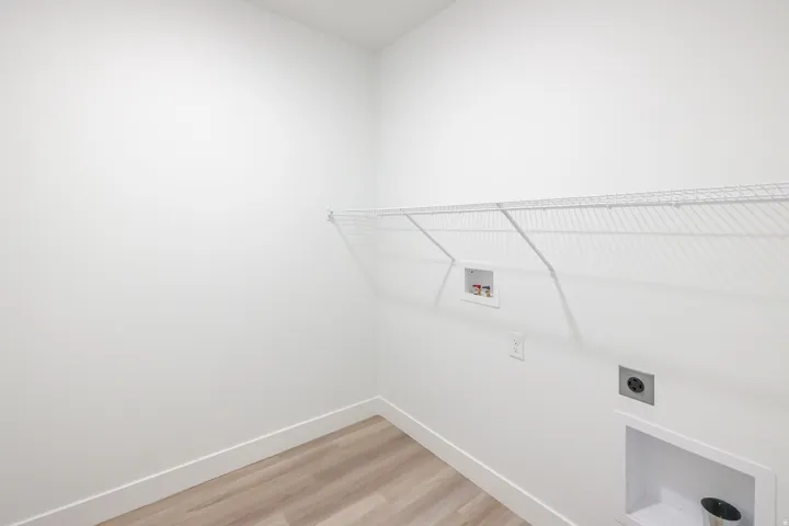 Laundry room featuring wood-finish flooring, white wire shelving, and utility hookups