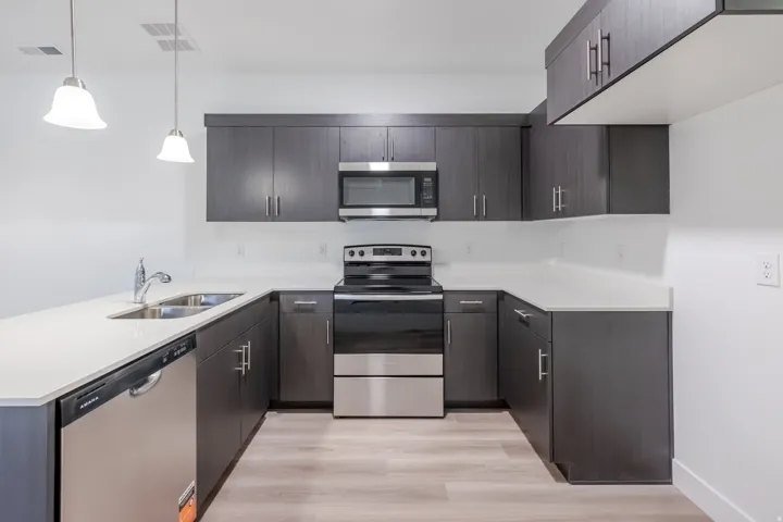 U-shaped kitchen featuring dark wood-finish cabinetry, light countertops, stainless steel appliances, and wood-finish flooring