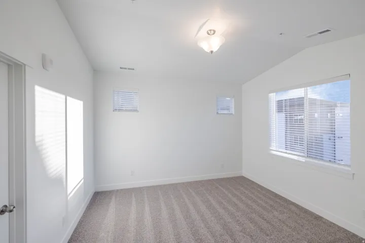 Carpeted flooring, vaulted ceiling, three windows with blinds, and flush mount lighting