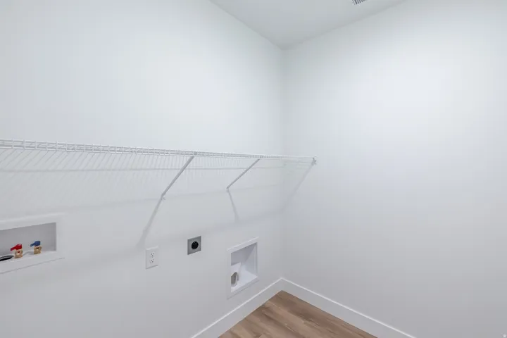 Laundry area featuring wood-finish flooring, white walls, and a white wire shelf