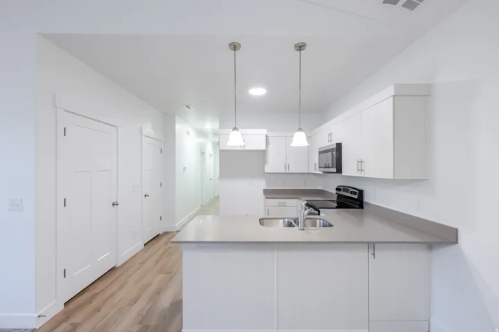 Modern kitchen with white cabinetry, light countertops, stainless steel sink, and wood-finish flooring