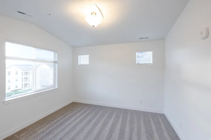 White walls with textured carpet flooring, large window with blinds, additional smaller windows, and a flush mount light fixture