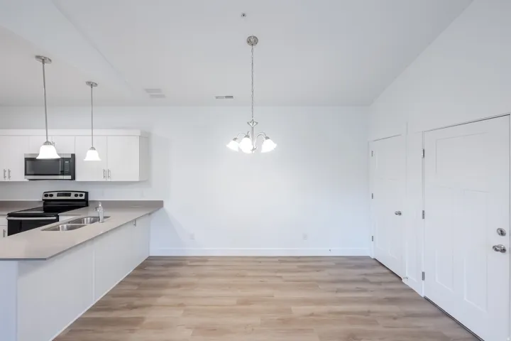 Open-concept kitchen and dining area with wood-finish flooring, white cabinetry, integrated stainless steel appliances, and a double basin sink