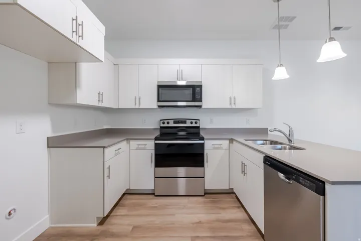 U-shaped kitchen with white cabinetry and grey countertops, stainless steel appliances, and wood-finish flooring
