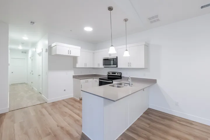 Modern kitchen featuring white cabinetry, light-toned countertops, stainless steel appliances, and wood-finish flooring