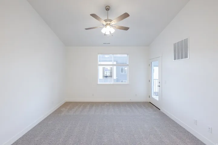 High ceilings, neutral carpeting, white walls, ceiling fan with integrated lighting, and a glass-paneled door