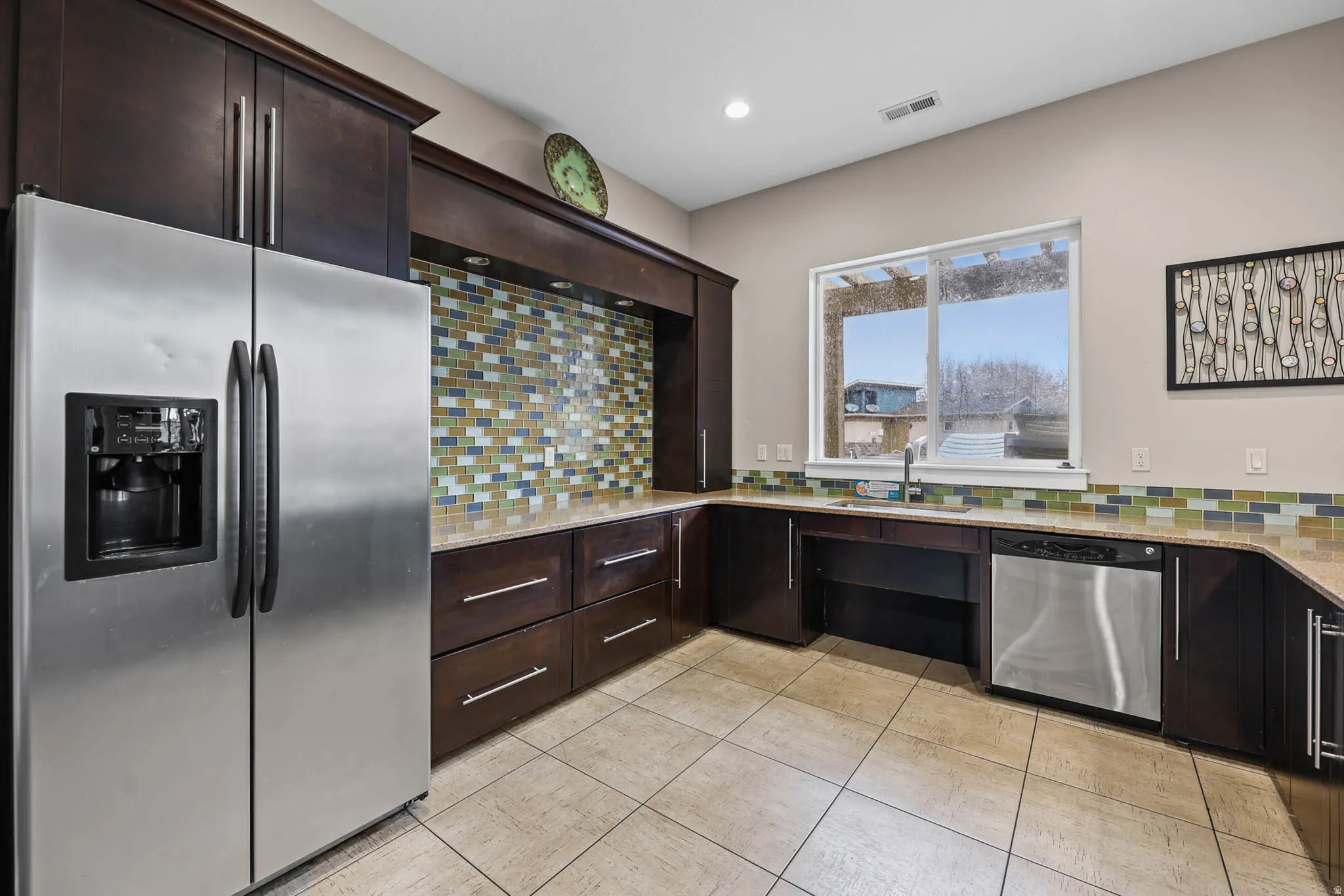 Kitchen featuring stainless steel appliances, dark wood finish cabinetry, light stone counters, decorative backsplash, and recessed lighting