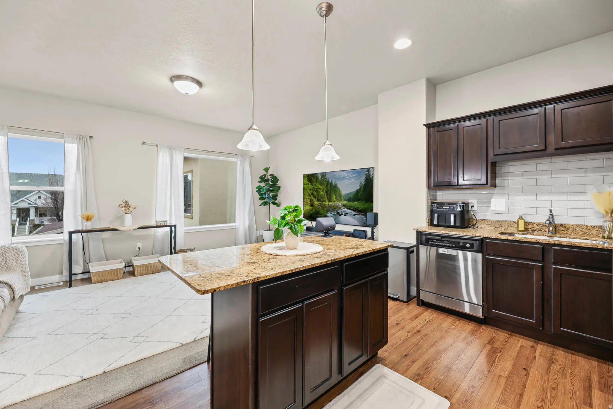 Kitchen featuring dark wood finish cabinets, light wood-style floors, light stone counters, and dishwasher