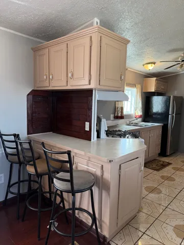 Kitchen featuring light countertops, a textured ceiling, a breakfast bar area, freestanding refrigerator, and ornamental molding