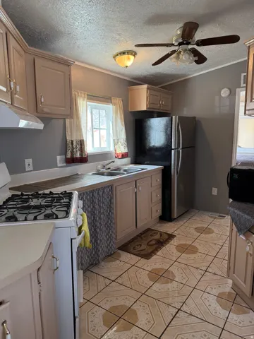 Kitchen featuring white gas stove, freestanding refrigerator, ornamental molding, a textured ceiling, and ceiling fan