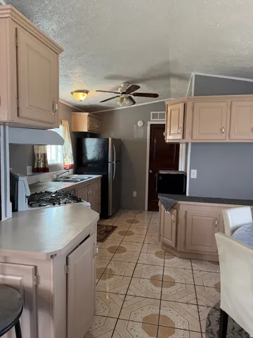 Kitchen featuring ceiling fan, freestanding refrigerator, range with gas cooktop, light countertops, and a peninsula
