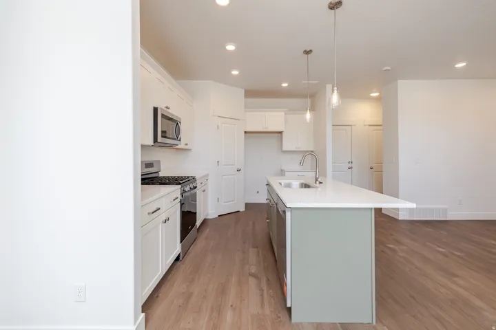 Modern kitchen featuring white cabinetry, stainless steel appliances, a center island with a sink, pendant lighting, and wood-finish flooring
