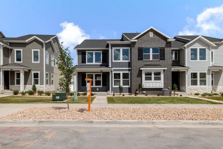 Contemporary townhome featuring a dark gray brick facade, contrasting white window trim, and a prominent front entrance with an overhang