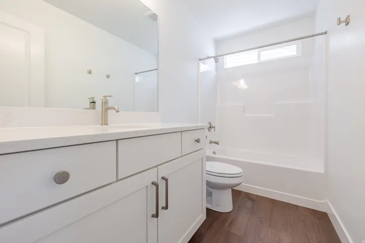 Bathroom featuring a white vanity with brushed nickel hardware, a white countertop, a rectangular undermount sink with a brushed nickel faucet, and a white tub/shower combination with a transom window