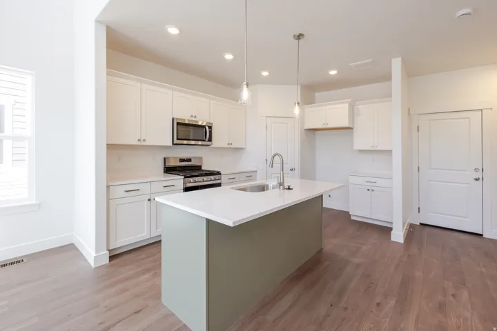 Kitchen featuring a central island with a contrasting base and integrated sink, stainless steel appliances, white cabinetry, and wood-finish flooring