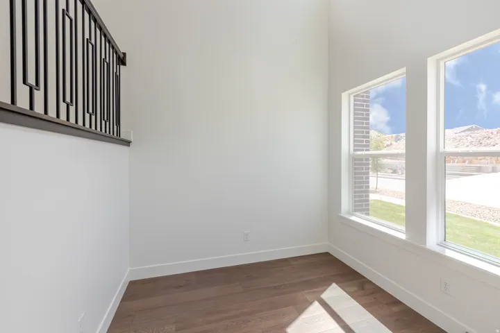 Wood-finish flooring with white baseboards, featuring two large windows with white trim, and a high ceiling