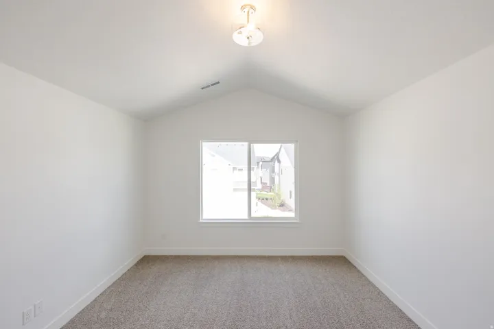 Vaulted ceilings enhance this room, featuring neutral carpeting and a single window with white trim