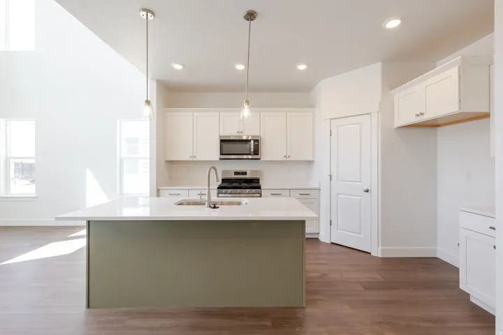 Modern kitchen featuring a central island with a contrasting base, a stainless steel sink with a gooseneck faucet, white shaker-style cabinetry, and wood-finish flooring