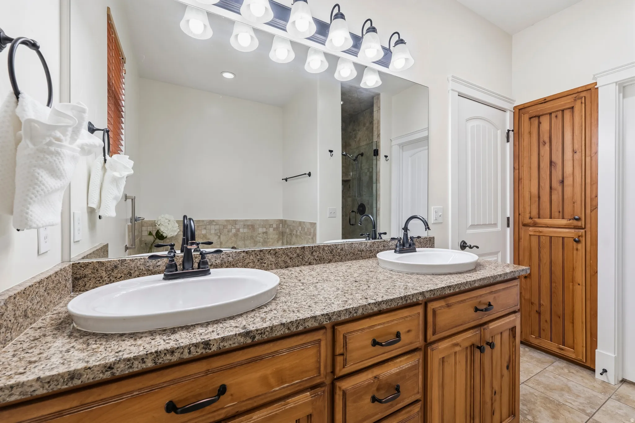 Bathroom with double vanity, a shower stall, and light tile patterned floors