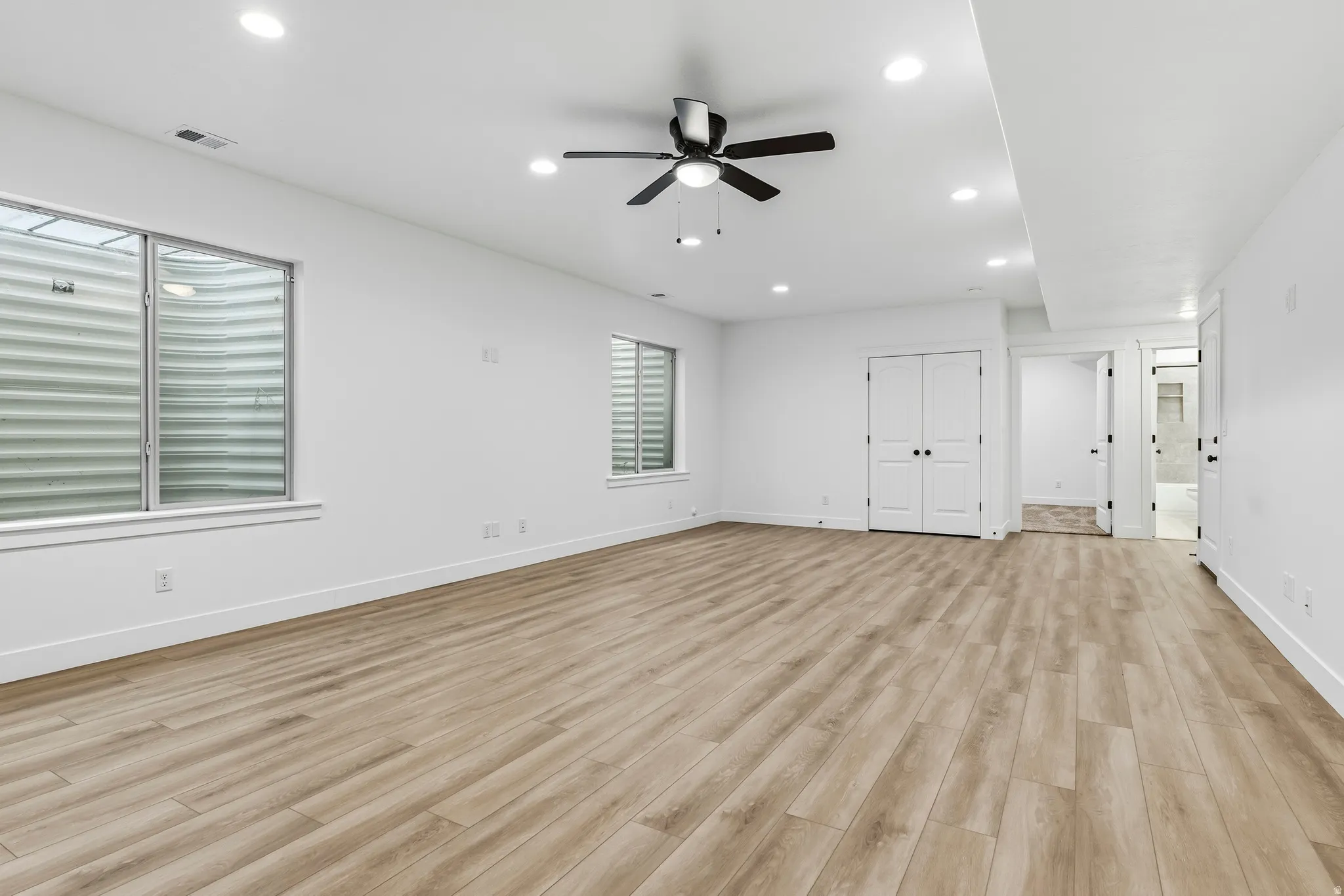Unfurnished bedroom featuring light wood-style floors, ensuite bath, recessed lighting, ceiling fan, and a closet