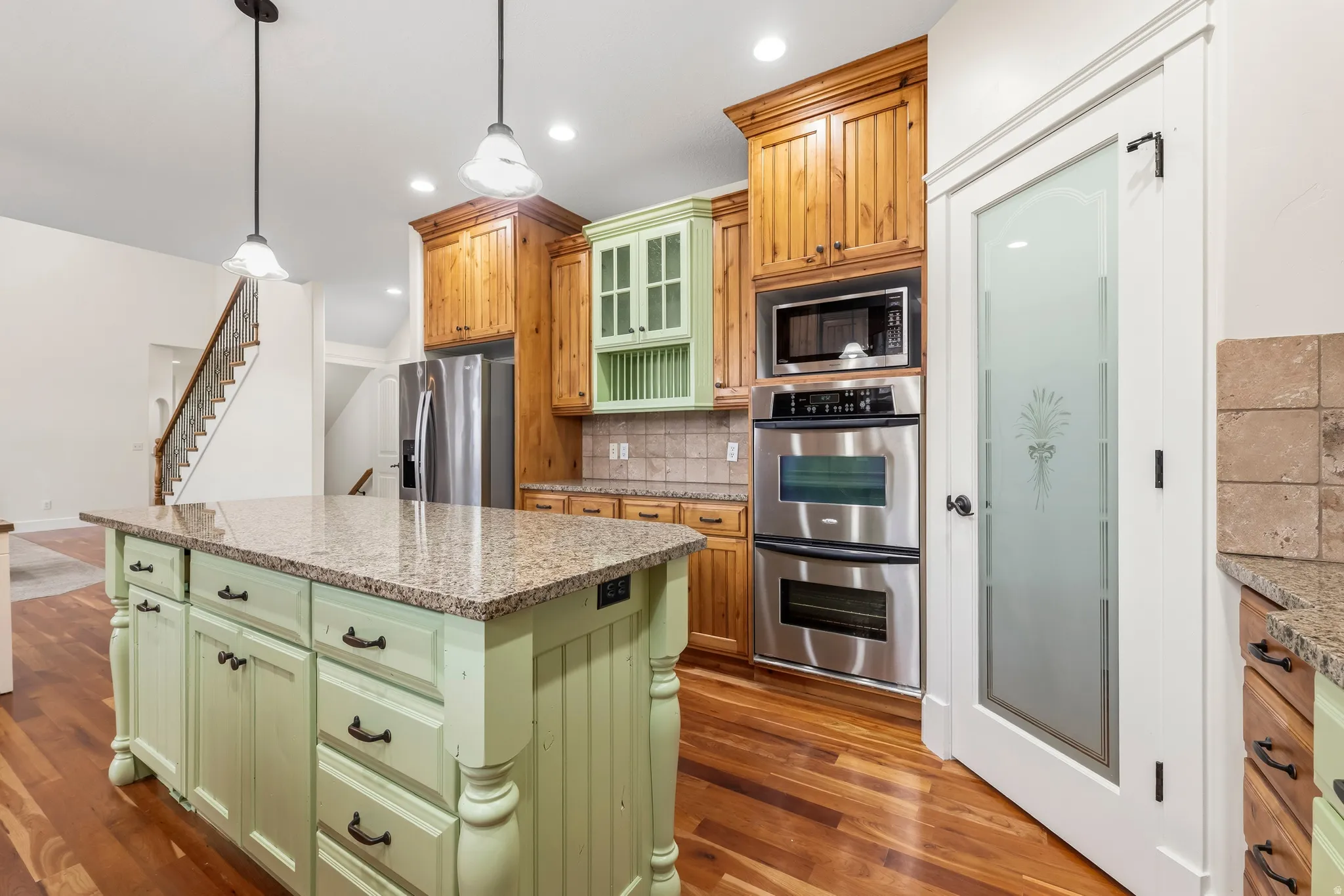 Kitchen with two tone cabinetry, glass insert cabinets, stainless steel appliances, light stone counters, and dark wood-style flooring
