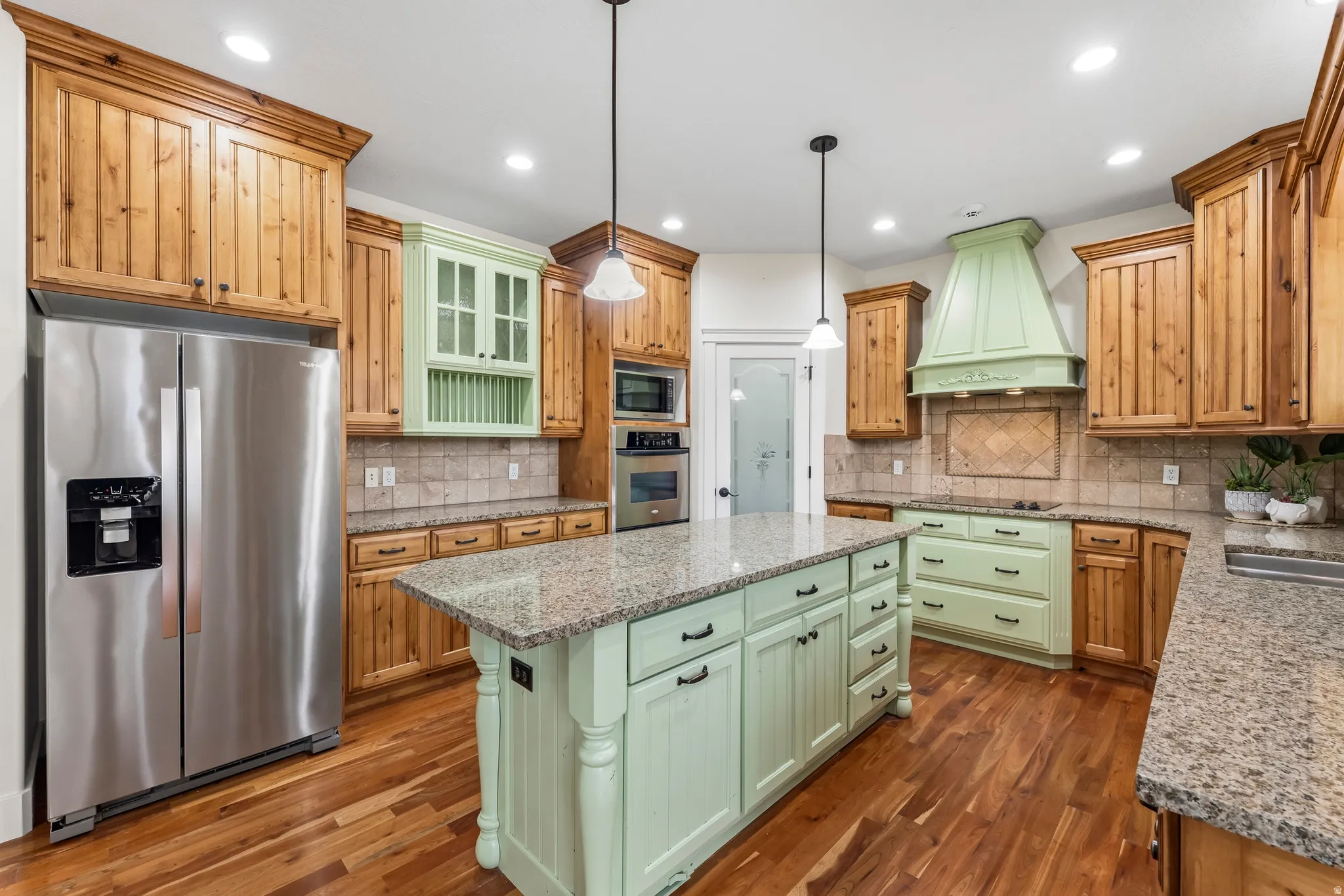 Two tone kitchen with stainless steel appliances, light stone countertops, a kitchen island, dark wood-style floors, and decorative light fixtures