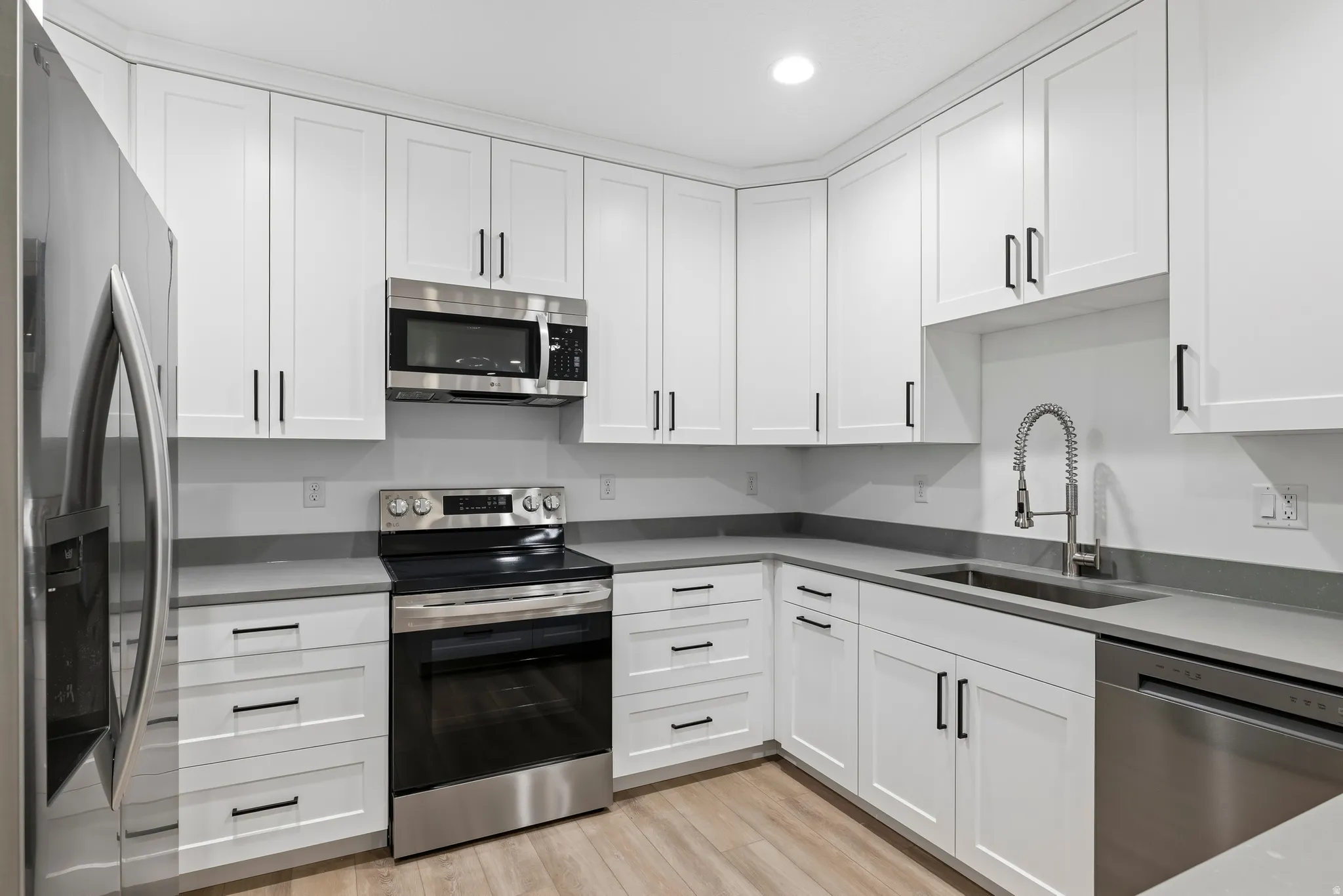 Kitchen with stainless steel appliances, white cabinets, light wood-type flooring, and recessed lighting