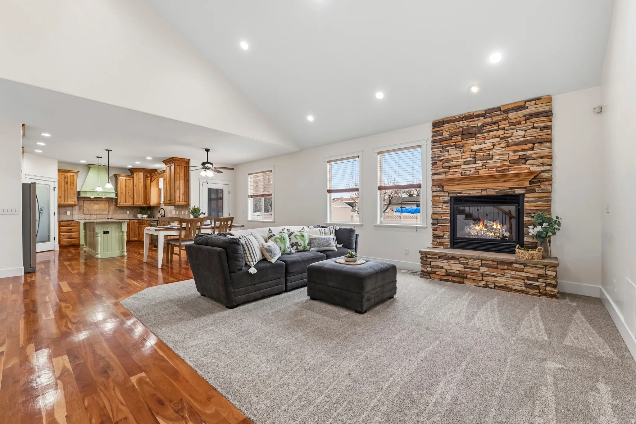 Living area with a stone fireplace, recessed lighting, lofted ceiling, ceiling fan, and dark wood finished floors