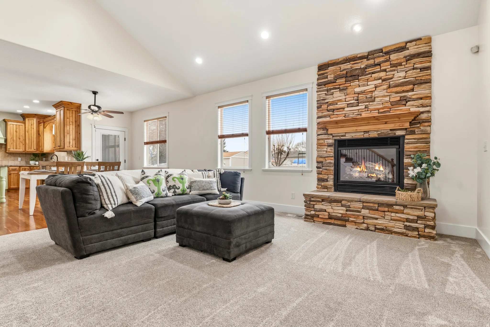 Living room featuring light carpet, a stone fireplace, recessed lighting, lofted ceiling, and ceiling fan