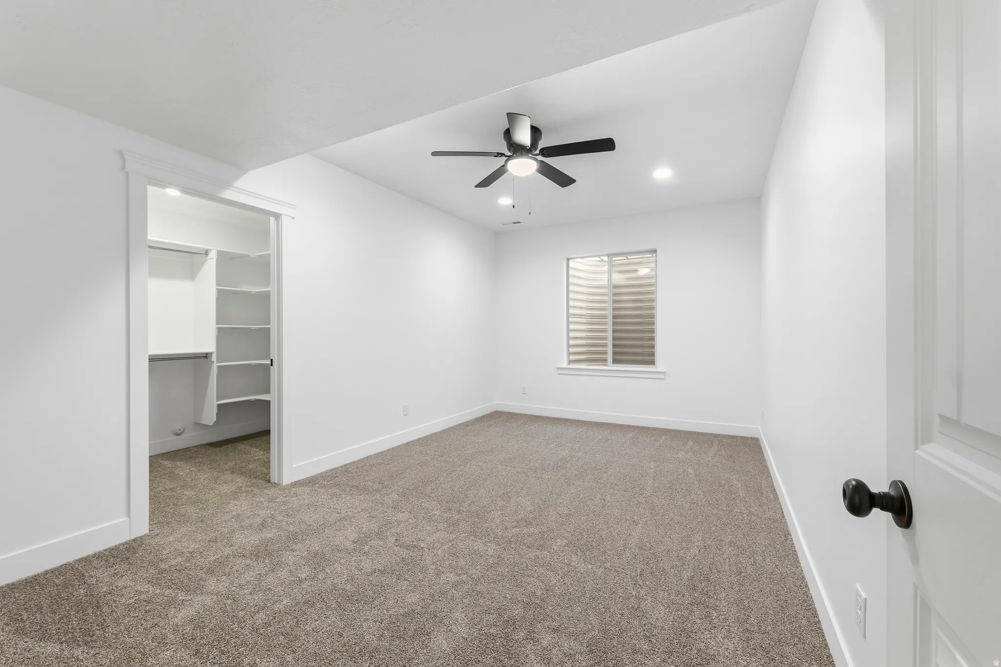 Unfurnished bedroom featuring carpet, a walk in closet, a ceiling fan, and recessed lighting