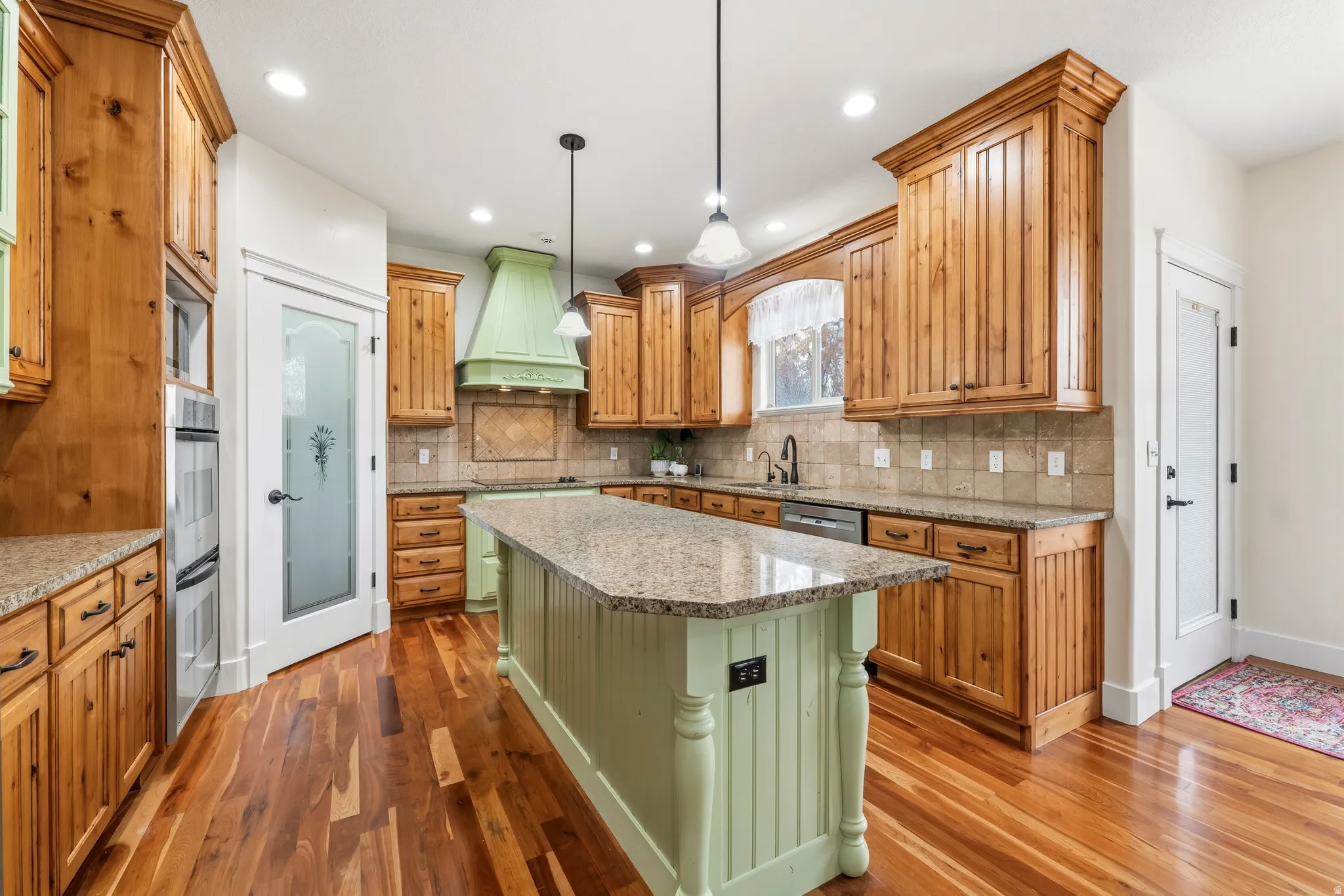 Two tone kitchen with light stone counters, two tone cabinets, light wood-type flooring, a kitchen island, and decorative light fixtures