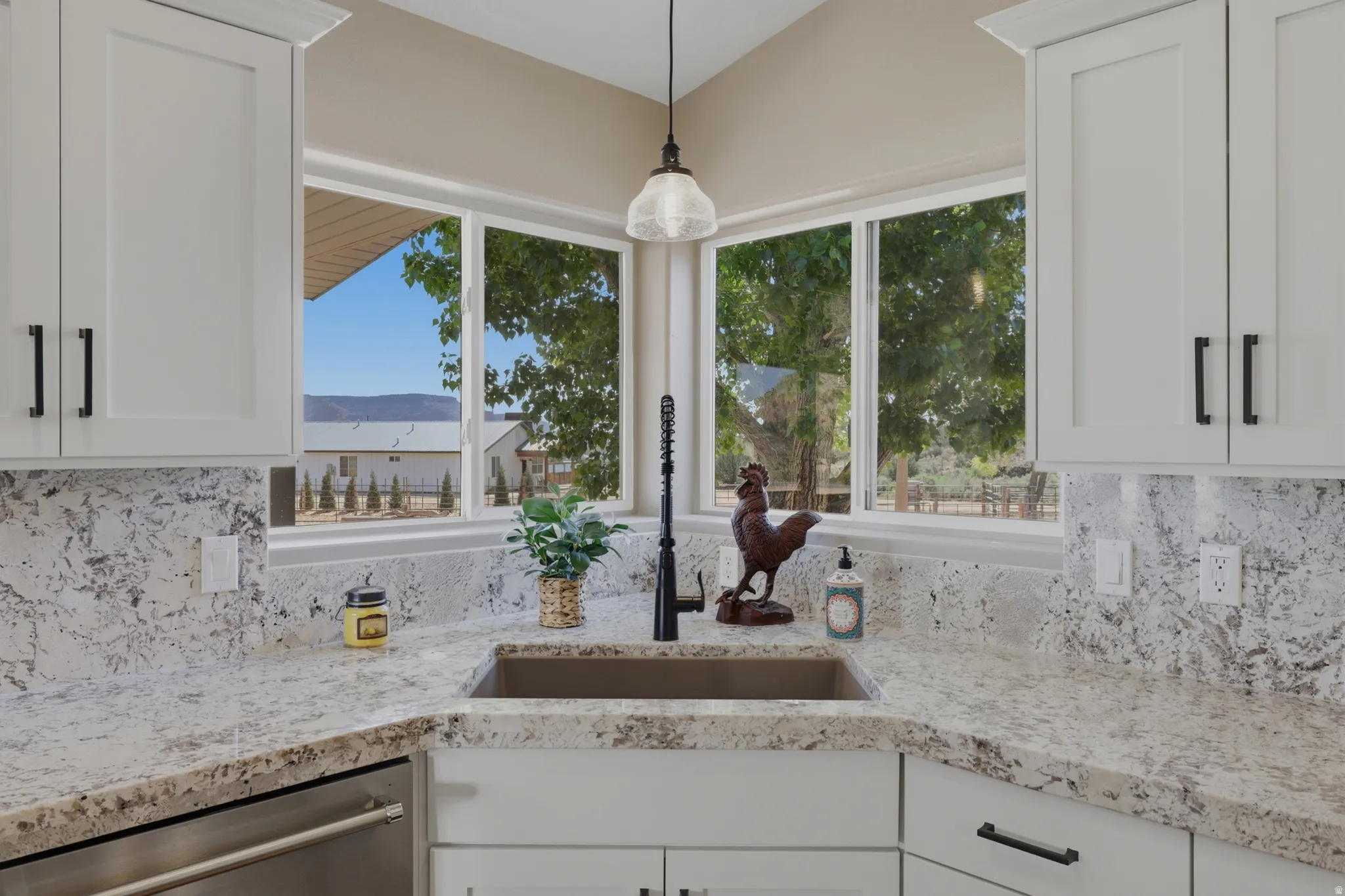Kitchen with light stone countertops, white cabinets, dishwasher, and hanging light fixtures