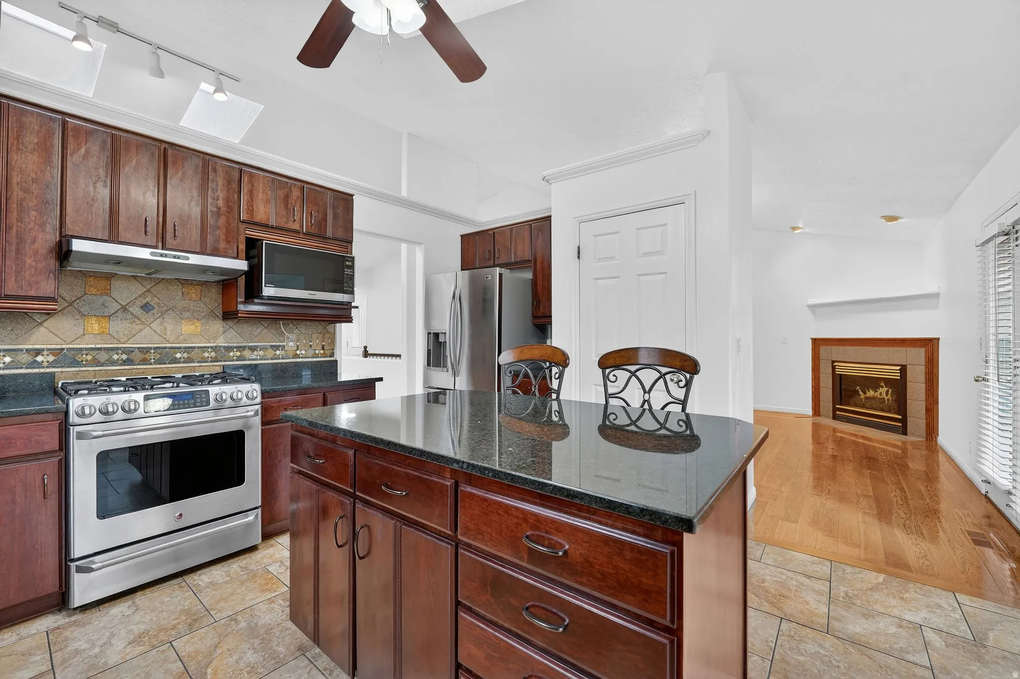 Kitchen featuring stainless steel appliances, a center island, a tile fireplace, dark stone counters, and backsplash