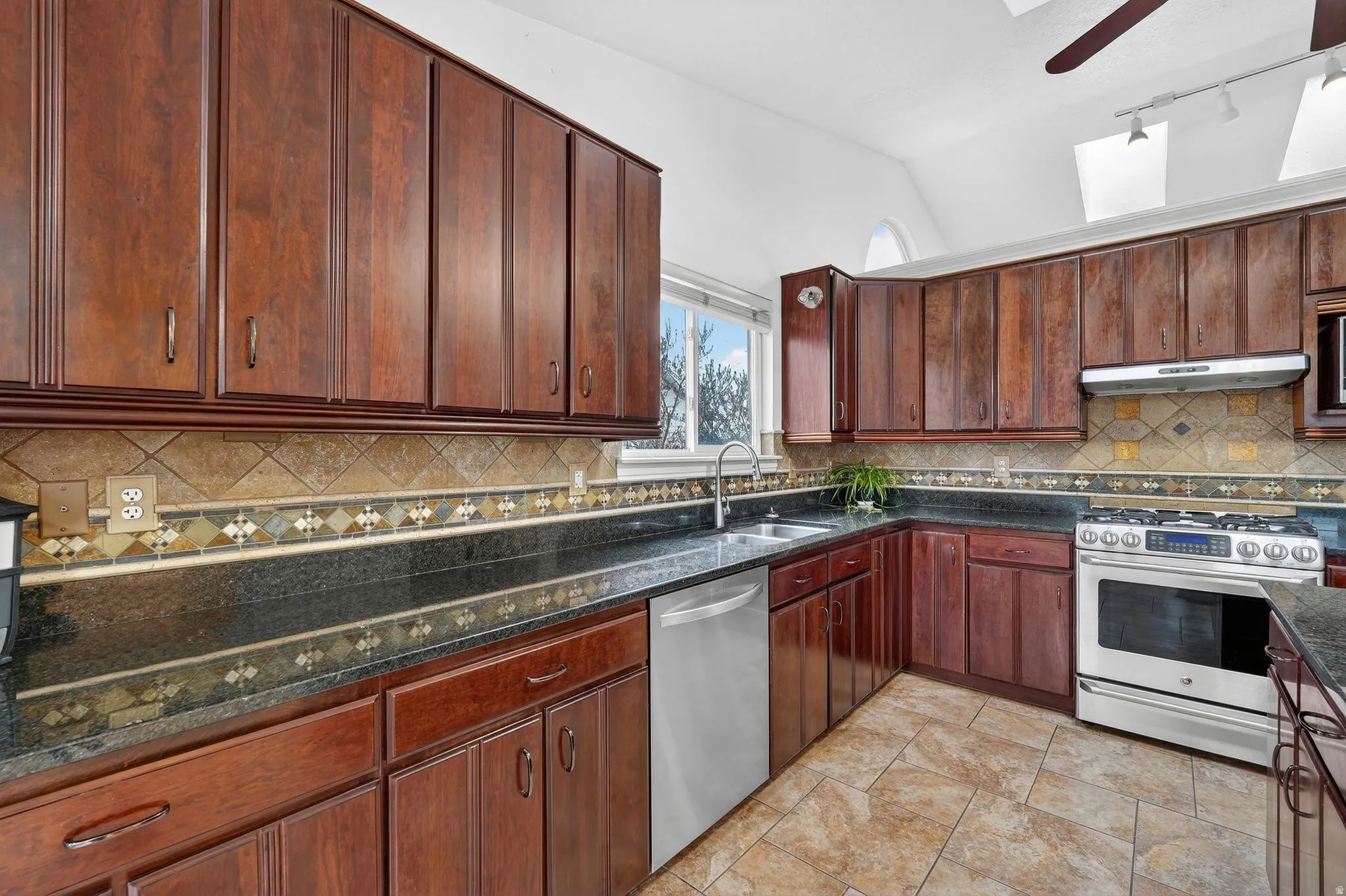 Kitchen featuring vaulted ceiling, stainless steel appliances, a skylight, rail lighting, and ceiling fan