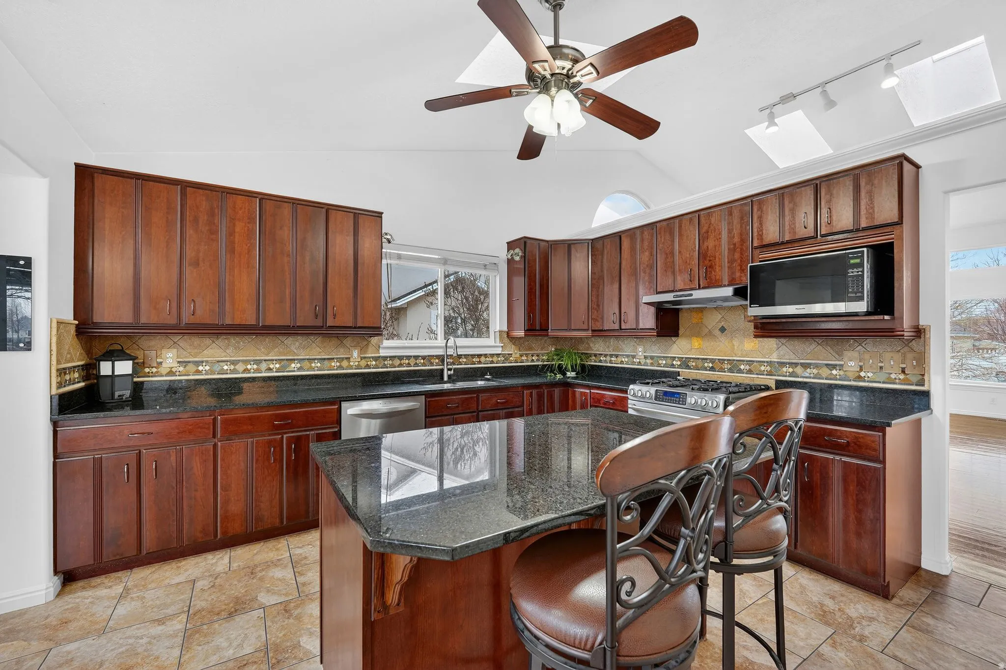 Kitchen featuring a breakfast bar area, vaulted ceiling, stainless steel appliances, dark stone countertops, and ceiling fan