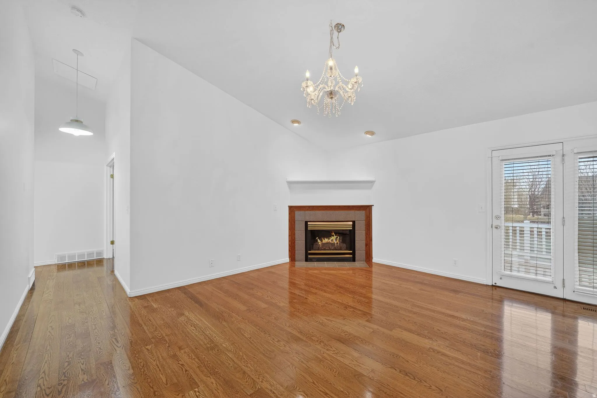 Unfurnished living room with a tile fireplace, lofted ceiling, light wood-style floors, and suspended lighting