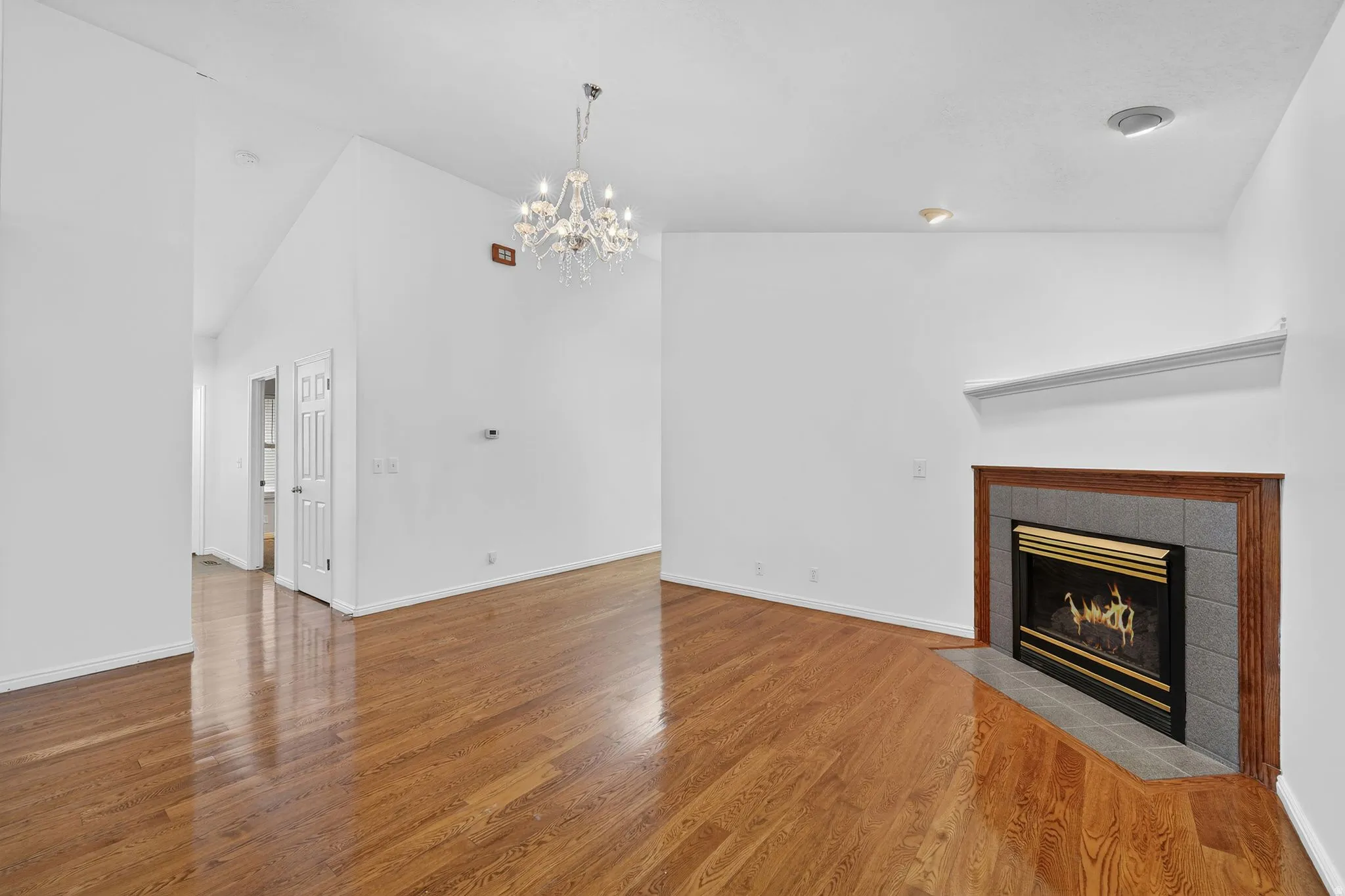 Unfurnished living room featuring a chandelier, a tile fireplace, light wood finished floors, and lofted ceiling