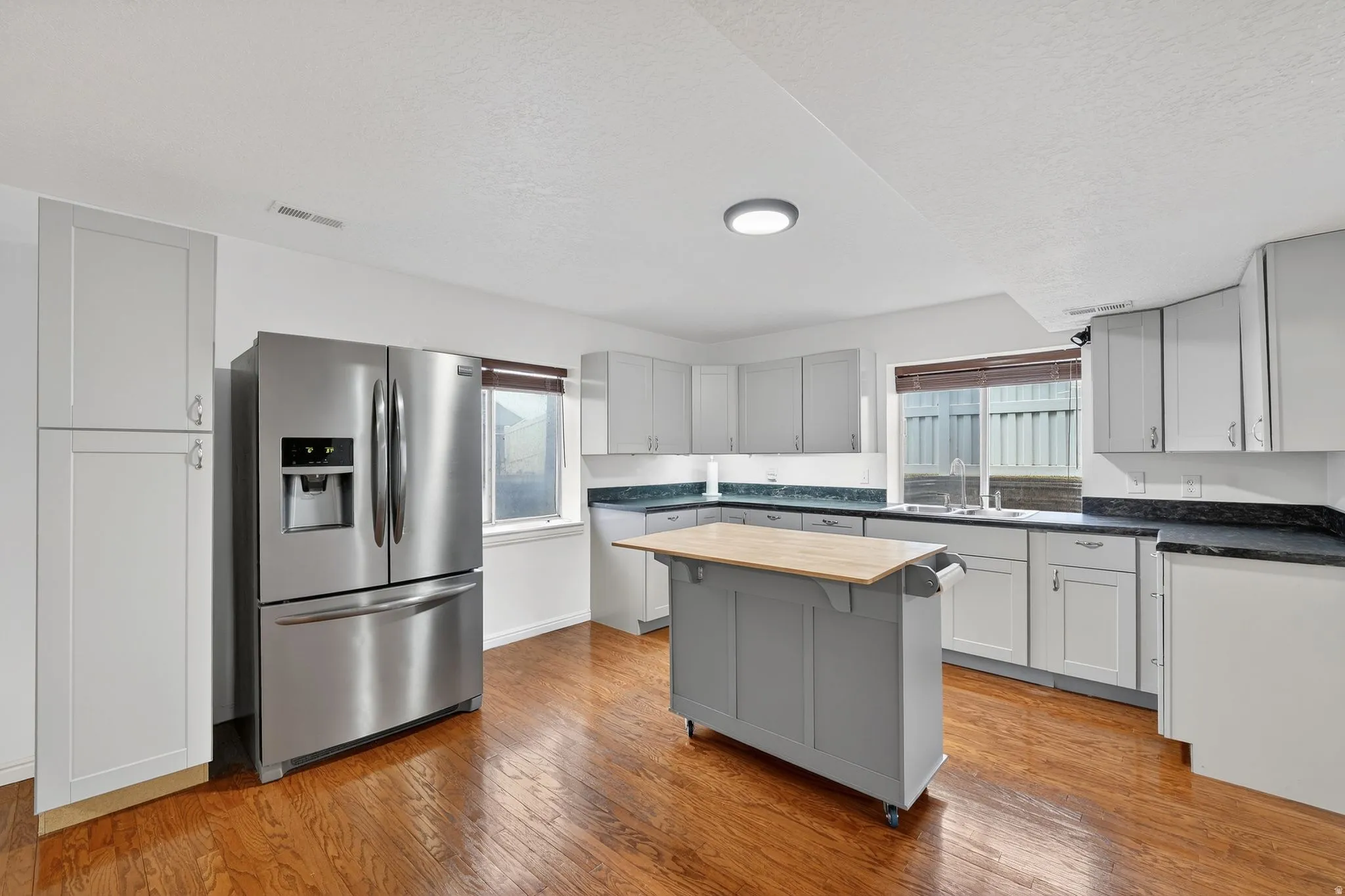 Kitchen with stainless steel fridge, light wood-style flooring, gray cabinets, a kitchen island, and butcher block countertops