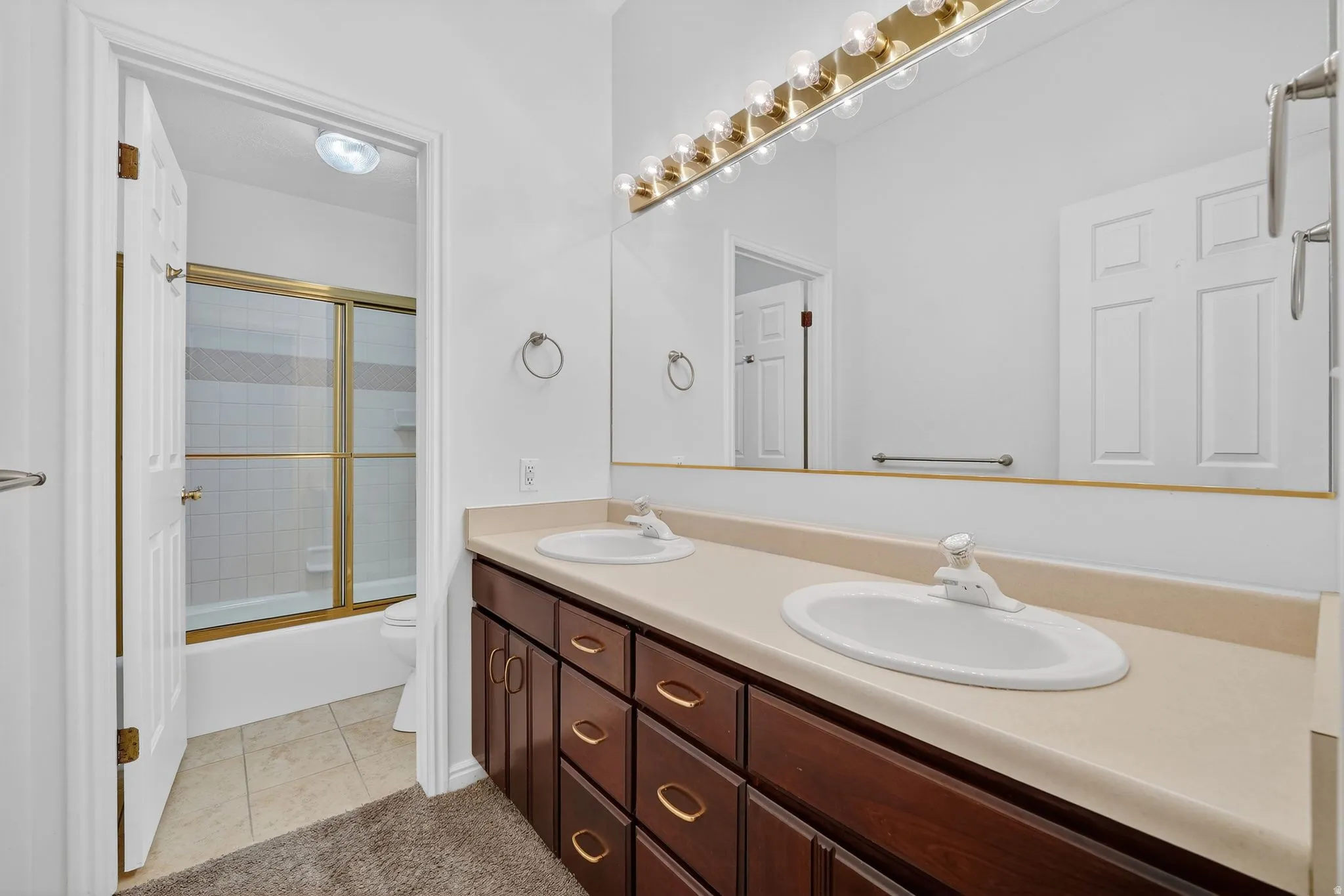 Full bath featuring double vanity, enclosed tub / shower combo, and light tile patterned floors